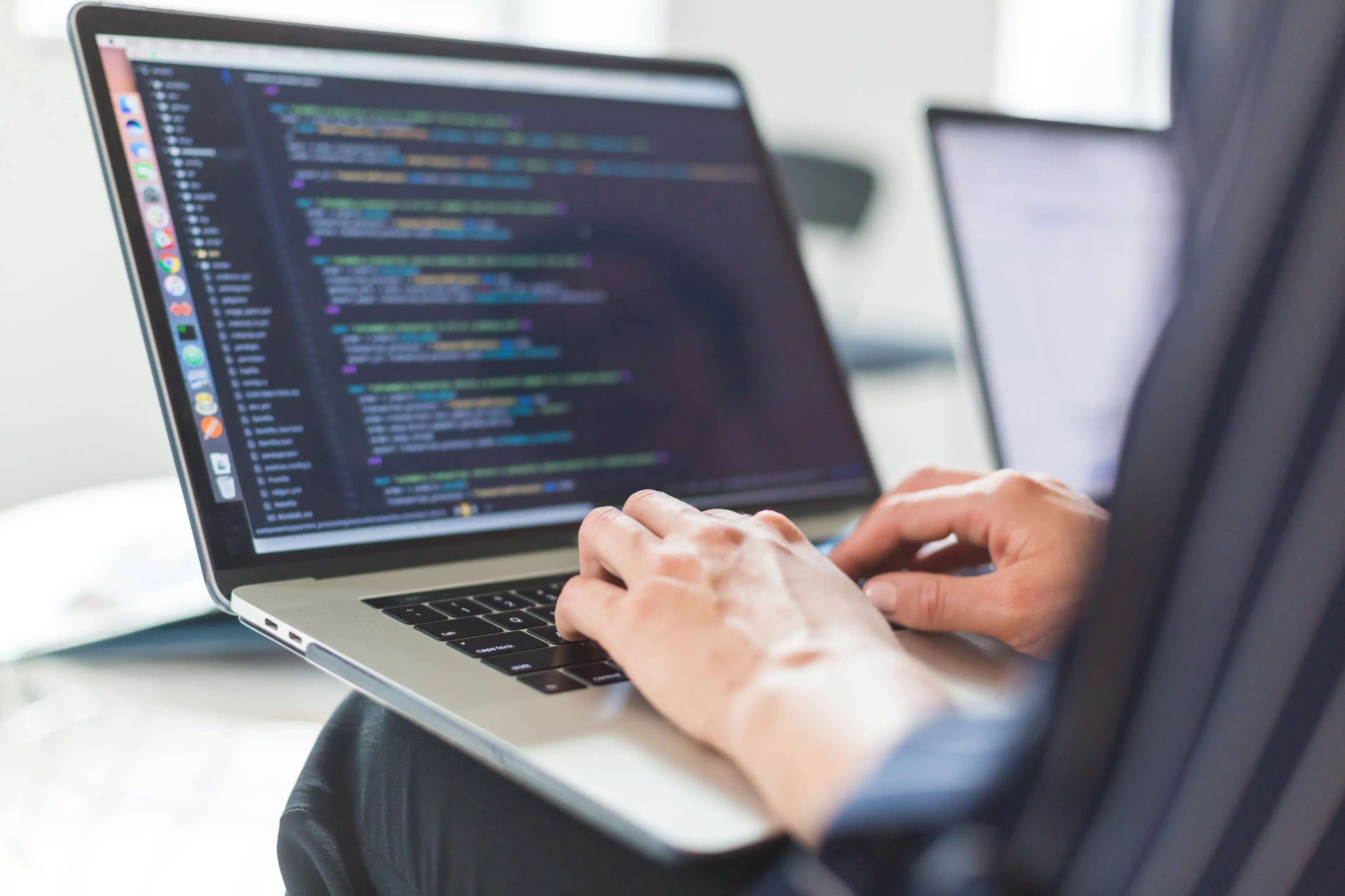 Person holds laptop on knees and types some code